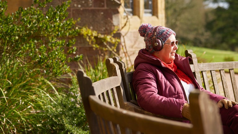 Visitor sat on a bench listening to headphones at Knightshayes, Devon